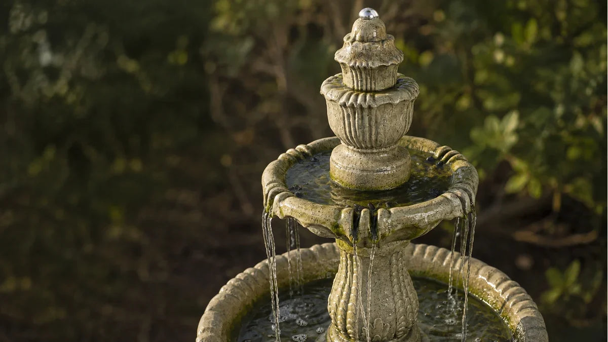 A scalloped concrete fountain tier with green algae film on the waterline and the wet stone above it
