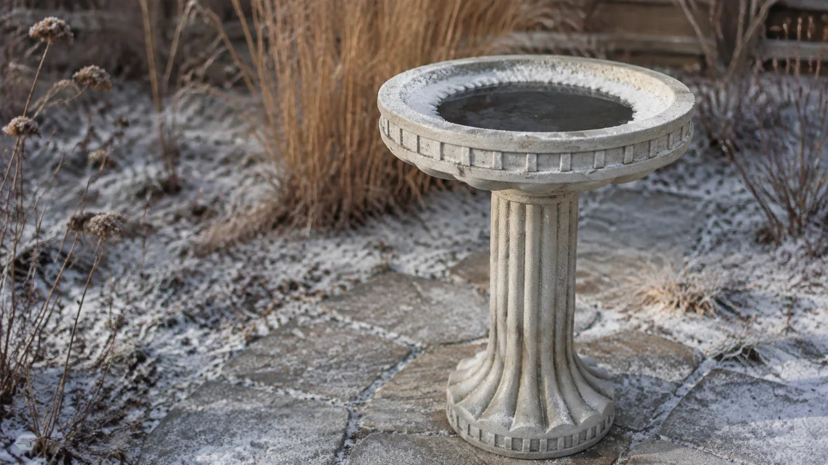 A fluted concrete bird bath in winter with ice around the rim and open water in the centre