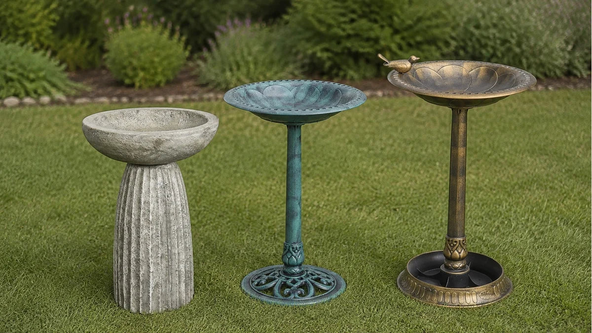 Three bird baths in rough concrete, green verdigris resin and antique bronze finish standing together on a lawn