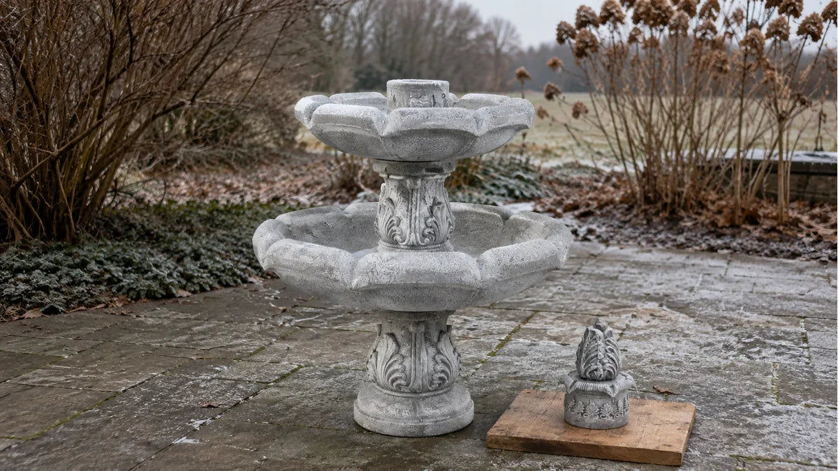 An ornate concrete fountain with its top tier removed and set on the ground, drained for winter