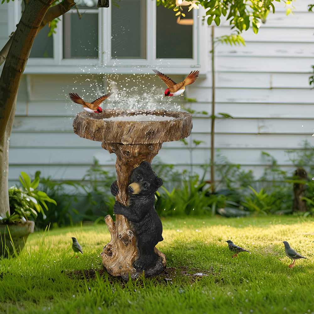 A bird bathing in a rustic black bear tree stump bird bath on a green lawn.