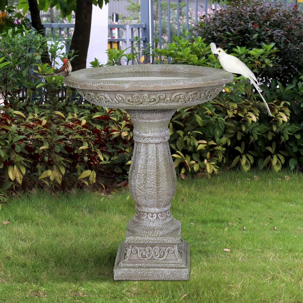 Antique stone-like fiber reinforced concrete birdbath in a backyard