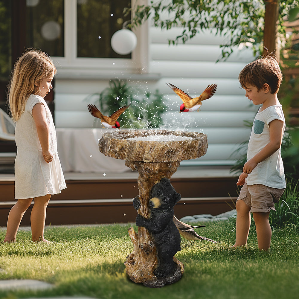 Children watching wild birds fly around a black bear tree stump bird bath in a garden.
