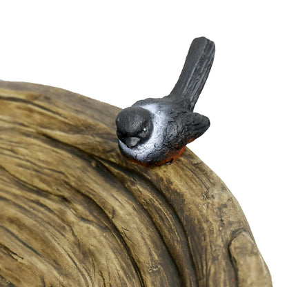 Close-up of the decorative black faux bird accent on the edge of the rustic tree trunk birdbath bowl.