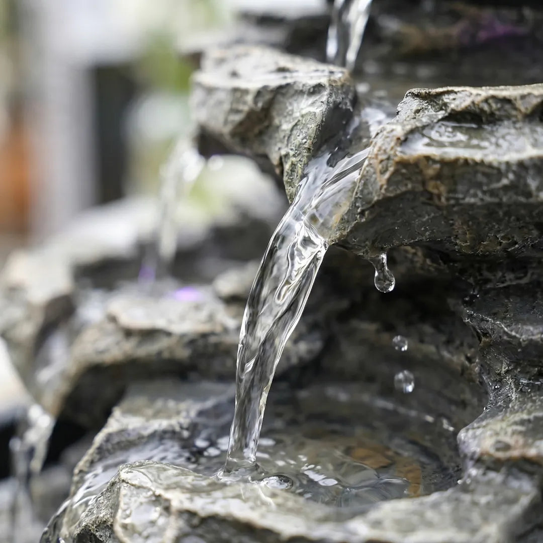 Close-up of water cascading smoothly over stone tiers of a tabletop fountain.