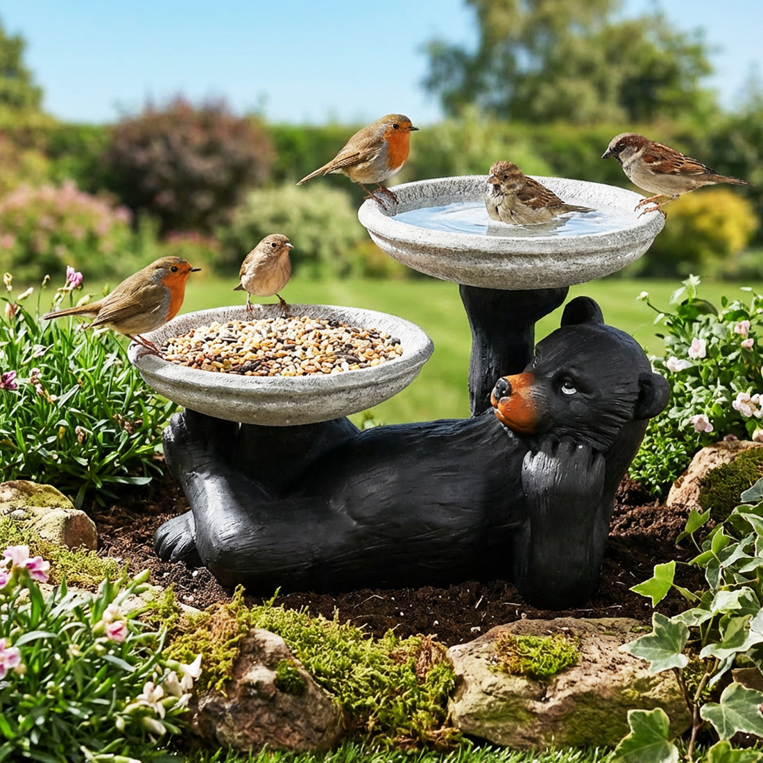 Double bowl black bear statue used as both a bird bath and feeder in a lush backyard.