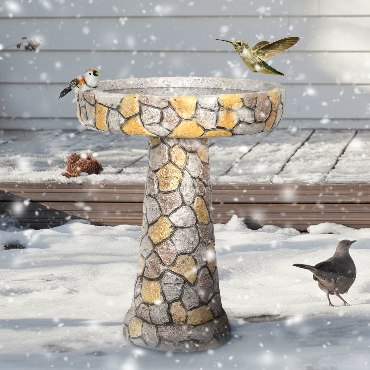 Mosaic stone style birdbath with birds on a snowy day in front of a house door.
