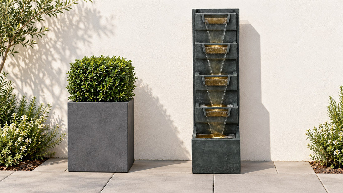 Modern cascade column fountain set level on pavers against a plain stucco wall beside a square planter
